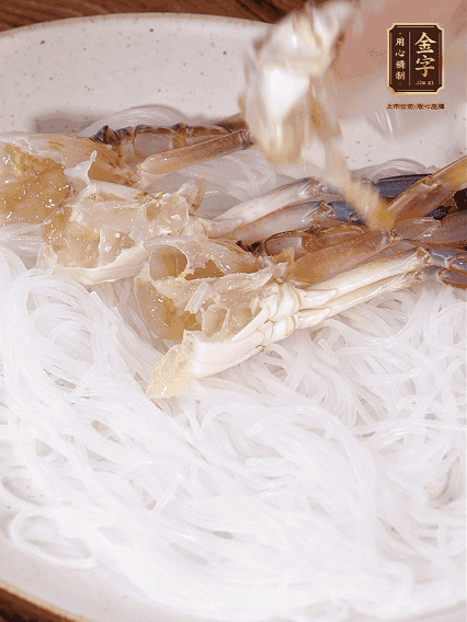 盤底墊上粉絲，擺上梭子蟹、火腿片，撒姜粒，淋上蒸魚豉油、花雕酒調(diào)味腌制15分鐘